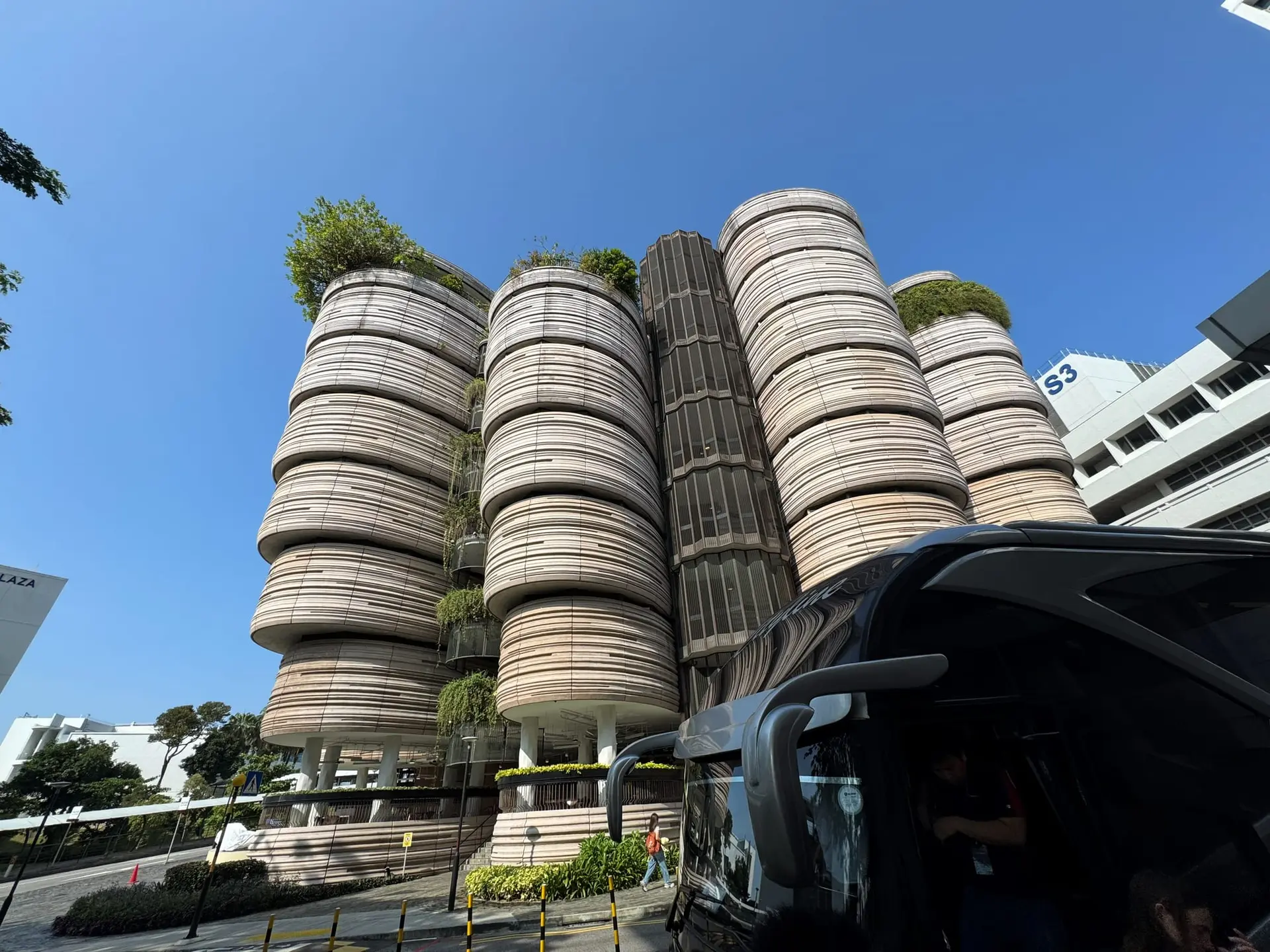 The Hive at Nanyang Technological University: stacked, rounded towers with plants growing on top, with a coach in the foreground