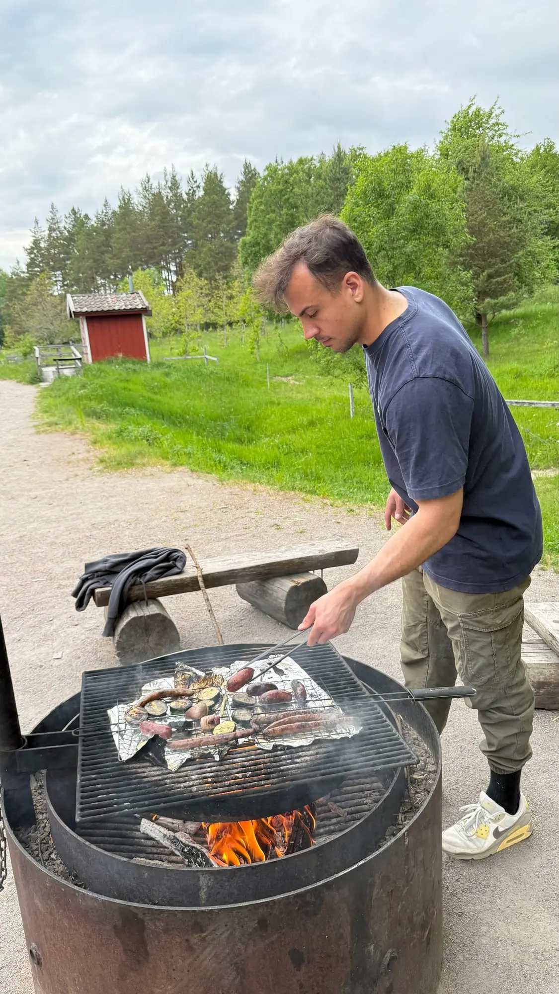 Dominik grilling sausages and vegetables over an outdoor fire pit in Sweden